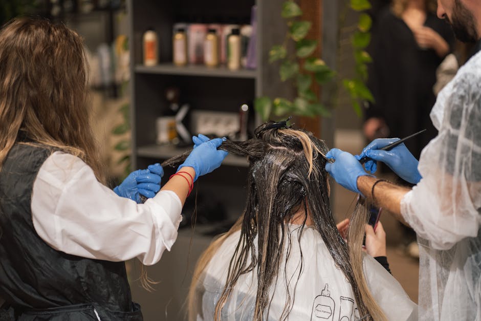 Professional stylists dyeing a woman's hair in a modern salon setting, showcasing teamwork and expertise.